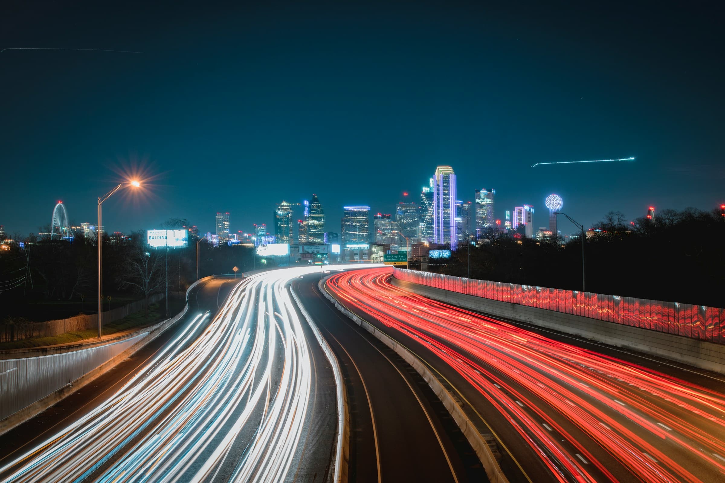 Highway light trails leading into the Dallas skyline at night
